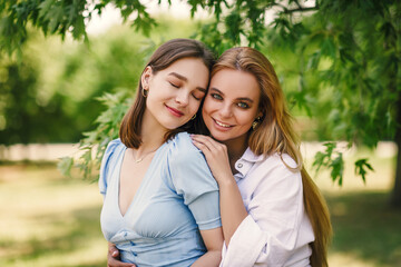 Obraz premium Two beautiful girls have fun in the park on a sunny summer day. The sisters are sitting on a green lawn, laughing.