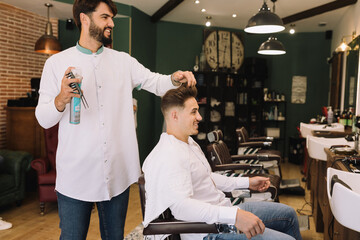 Fototapeta na wymiar handsome barber combing a young brown man's hair at the barber shop with hairspray