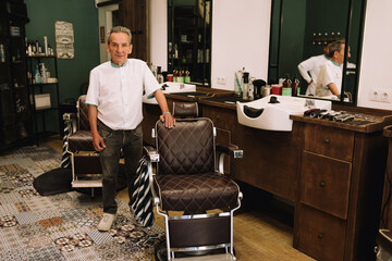Friendly and expert barber looking at the camera standing and smiling.  Man in hairdressing salon .