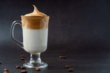 Glass of trendy fluffy creamy dalgona or whipped instant coffee with milk and coffee beans on the dark background. New popular food and drink trend concept. Copy space.