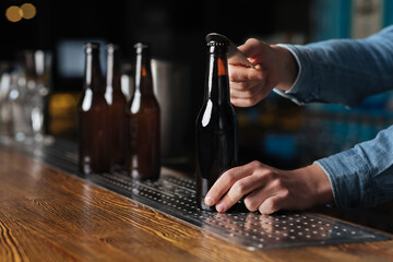 Bartender hands open bottle of beer in a dark bar interior