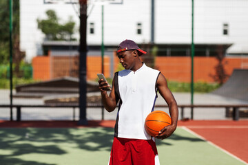 Black athlete browsing web on cellphone before basketball game at outdoor arena