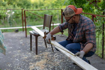 Handsome young man carpenter installing a wood fence outdoor terrace in new house. Wearing safety glases and gloves , using measuring tape