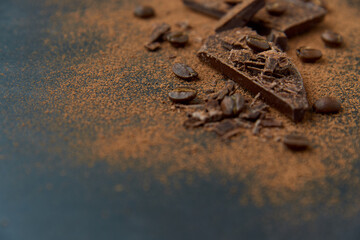 Dark chocolate stack, chips and cocoa powder with coffee beans on a dark background. Confectionery and food concept. Top view, copy space, selective focus..