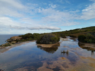 Beautiful coastal trail with colorful rock formations and reflections of blue sky on water puddles near Wattamolla Beach, Royal National Park, New South Wales, Australia