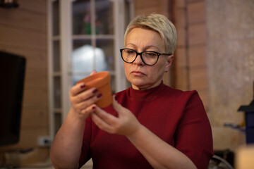 Beautiful adult woman holding clay ceramic pot in hands, blank for painted handmade gift, art home studio workspace, lifestyle, fous on artist. Handmade pot, DIY, creative pottery workshop