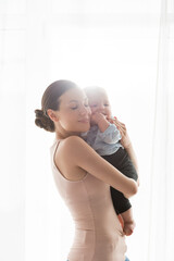 smiling mother with closed eyes holding in arms adorable infant son in baby clothing