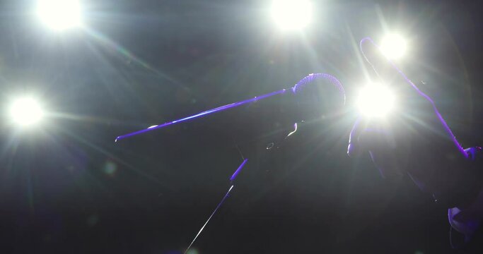 Man is checking microphone, he is knocking softly on mic using fingers. Hand of man testing microphone on stage in spotlight in dark preparing to performance.