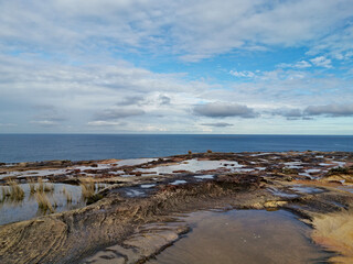 Beautiful coastal trail with colorful rock formations and reflections of blue sky on water puddles near Wattamolla Beach, Royal National Park, New South Wales, Australia