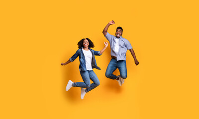 Fototapeta na wymiar Crazy Sales. Cheerful Black Couple Jumping High In Air Over Yellow Background