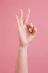 Female hand showing OK gesture, isolated on  pink background.
