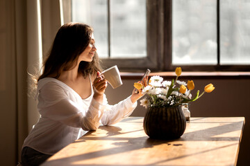 Young woman with cup of coffee is stare at the phone at kitchen 
