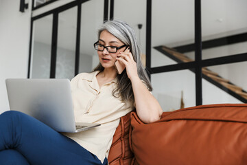 Photo of asian woman talking on mobile phone while working with laptop