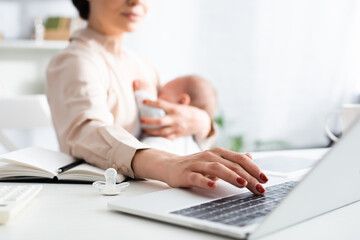 Fototapeta premium selective focus of mother breastfeeding infant son while working from home with laptop