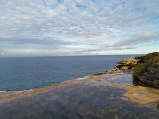 Beautiful coastal trail with colorful rock formations and reflections of blue sky on water puddles near Wattamolla Beach, Royal National Park, New South Wales, Australia