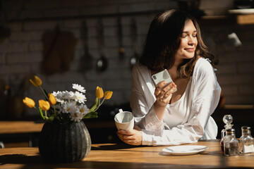 Young woman with cup of coffee is stare at the phone at kitchen 