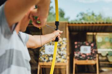 Archer holds yellow bow aiming at a target, during a open air corporate team building.  Outdoor leisure activity concept