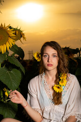 Beautiful young girl posing in a sunflower field at sunset 