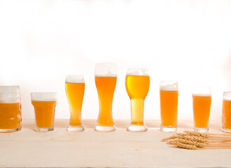 Glasses filled with beer in different shapes and sizes on bright white background 