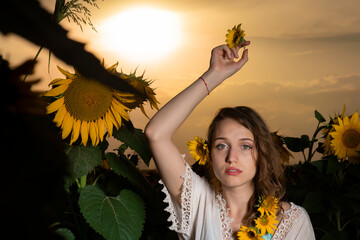 Beautiful young girl posing in a sunflower field at sunset 