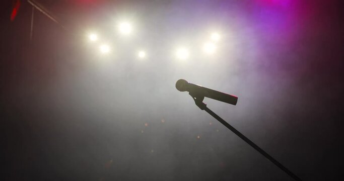 Professional concert microphone on stage for record or speak to audience in dark in the spotlight. Musical instrument concept, vocal equipment. Camera in motion, moving away.