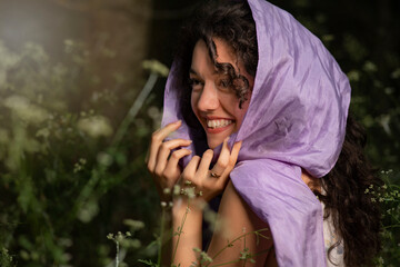 Happy young girl posing with a purple scarf on forest background