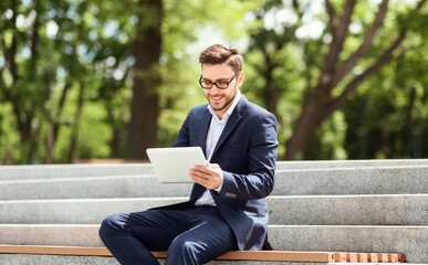Obraz premium Smiling young office employee working with tablet computer while sitting on stairs at city park