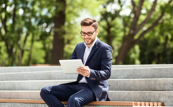 Smiling young office employee working with tablet computer while sitting on stairs at city park