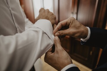 Selective focus shot of the groomsman helping groom to put on cufflinks