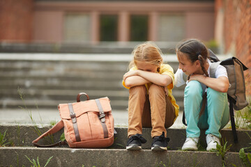 Full length portrait of teenage schoolgirl crying while sitting on stairs outdoors with smiling...
