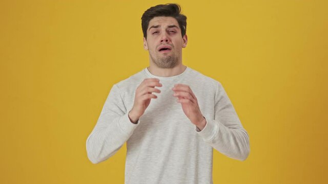 Unhappy sick man with runny nose sneezing and looking at the camera over yellow background