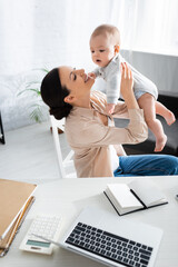 Obraz premium selective focus of happy mother holding in arms cute infant son near laptop