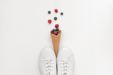 White women's sneakers and a horn with summer berries on a light background, close-up, minimal, art, modern. The concept is the enjoyment of quality shoes. Flat lay, top view