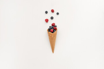 Bouquet of blueberries and raspberries in a waffle cone. Minimal style on a white background. The concept of delicious summer desserts and good nutrition.