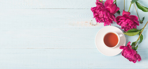 Red pink peonies tea cup on a blue wooden background. Horizontal frame copy space for text design. Top view