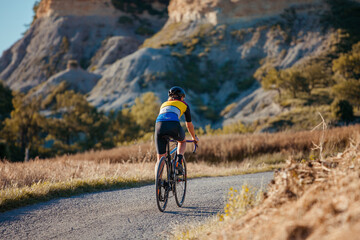 Fototapeta premium Back view of a cyclist girl pedaling on her bicycle in a beautiful countryside setting.