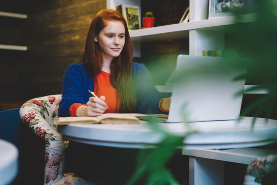 Charming carroty young female author searching useful information in websites for article publication on laptop computer connected to wireless internet,hipster girl chatting in social networks