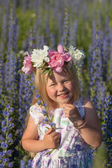 Obraz premium Little beautiful girl in a flower field on a sunny summer day during summer vacation. A girl with long hair smiles and laughs. Girl with a wreath on her head. Selective focus image.