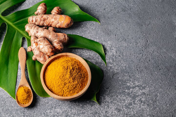 Turmeric powder and fresh turmeric root on grey concrete background.