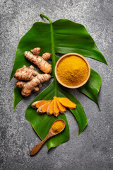 Turmeric powder and fresh turmeric root on grey concrete background.