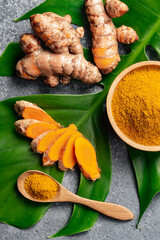 Turmeric powder and fresh turmeric root on grey concrete background.