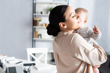 attractive mother holding in arms and hugging cute infant son in baby romper
