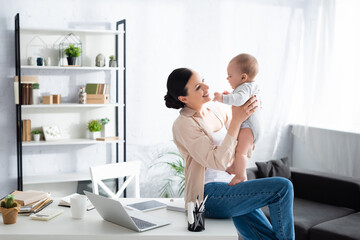 happy mother holding in arms cute infant son near gadgets and cup of table