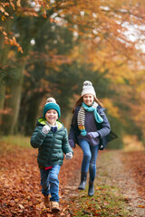 Portrait Of Two Smiling Children Having Fun Running Along Path Through Autumn Woodland Together