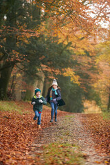 Two Smiling Children Having Fun Running Along Path Through Autumn Woodland Together