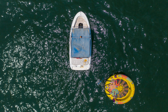 Small Boat with inflated Yellow donut wake ride attached by ski rope, Aerial image.