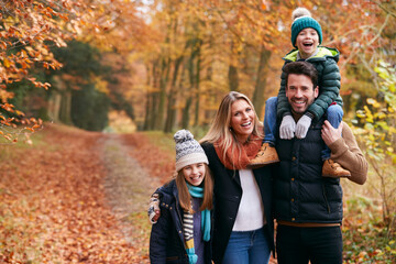 Portrait Of Family Walking Along Autumn Woodland Path With Father Carrying Son On Shoulders