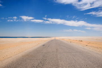 Long straight desert road towards the horizon. Low perspective, blue sky and white clouds. Desert landscape at Egypt, Africa. Adventure travel background. 