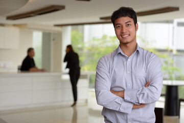 Happy young Asian businessman smiling with arms crossed in the office building