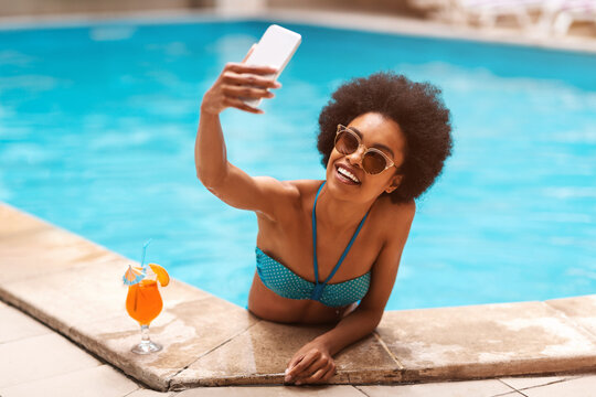 Pretty African American woman taking selfie while relaxing at pool on hot summer day